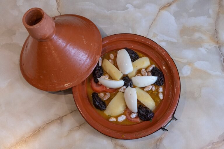 طبق تبغة مغربي ساخن يقدم في طاجين حجري، يحتوي على لحم بقري، بطاطس مطهية، وبيضة ناضجة فوق الصلصة الحمراء الغنية بالبهارات، مع رشة بقدونس أخضر.